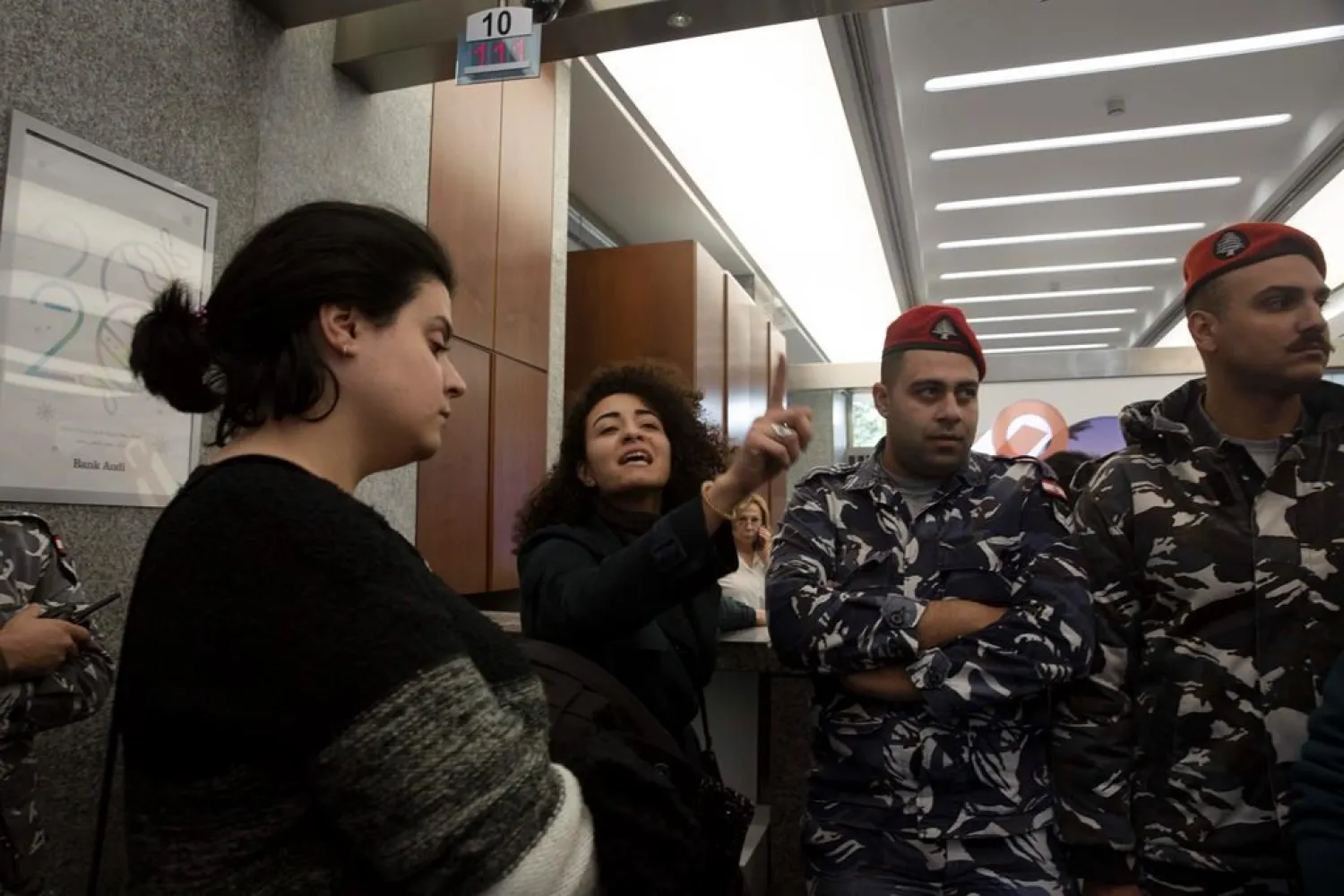 An anti-government protester shouts slogans as Lebanese police stand guard inside a branch of Bank Audi on Monday, Dec. 30, 2019 in Beirut. (AP)