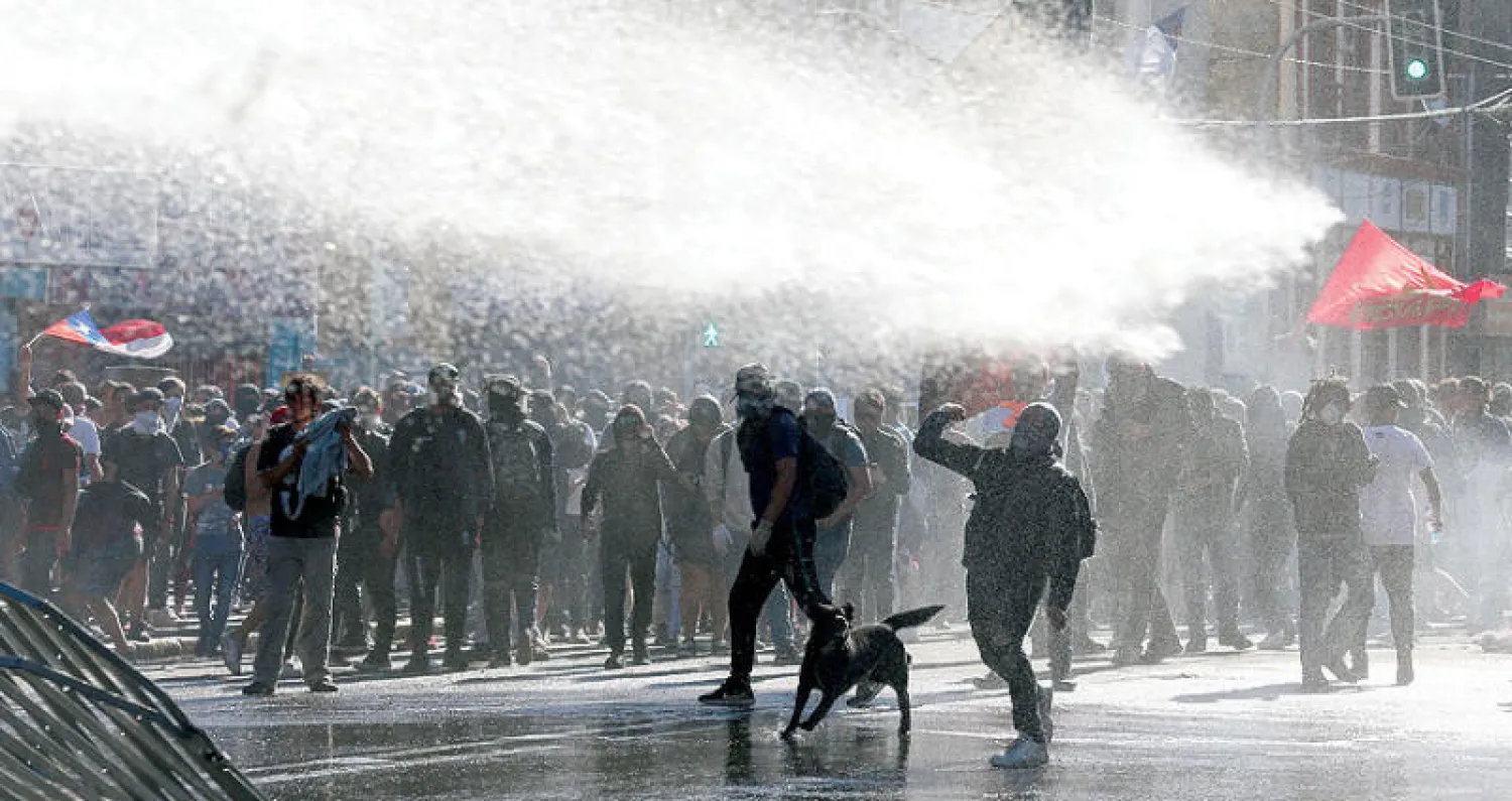 متظاهرون في تشيلي أثناء تعرضهم للمياه بخراطيم قوات الأمن لتفريقهم في أكتوبر الماضي (رويترز)