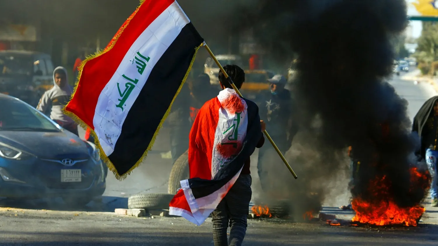 A demonstrator carries an Iraqi flag as he walks near burning tires, during ongoing anti-government protests, Najaf, Iraq, Jan. 12, 2020. (Reuters)