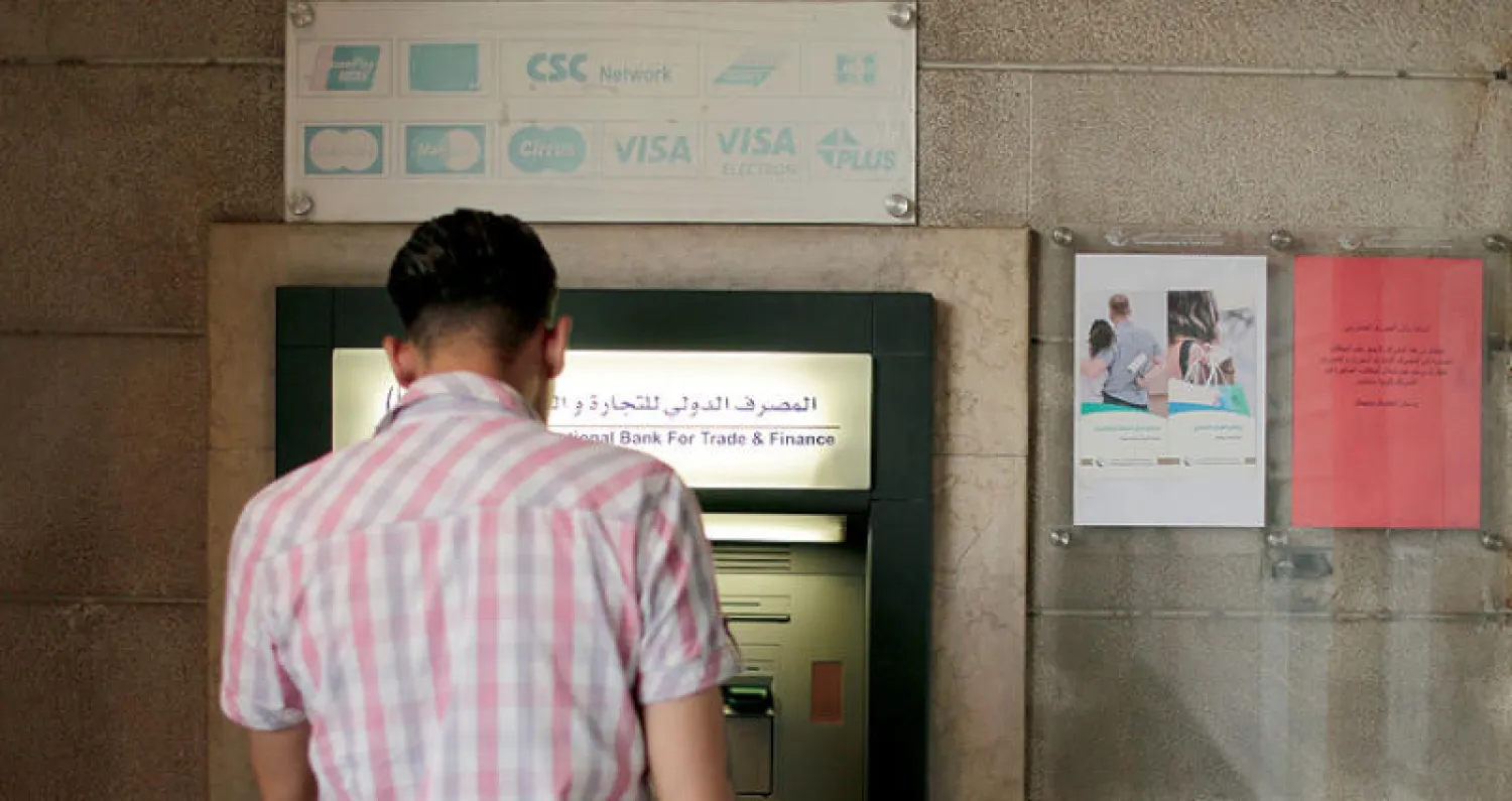 سوري أمام آلة لسحب الأوراق النقدية في دمشق (إ.ب.أ)