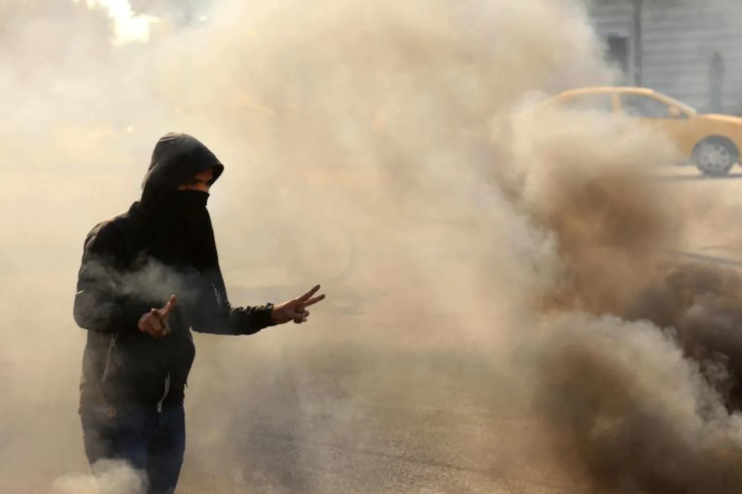 متظاهر ملثم يشير بعلامة النصر وهو يركض من الغاز المسيل للدموع  خلال اشتباكات في مدينة كربلاء (ا.ف.ب)