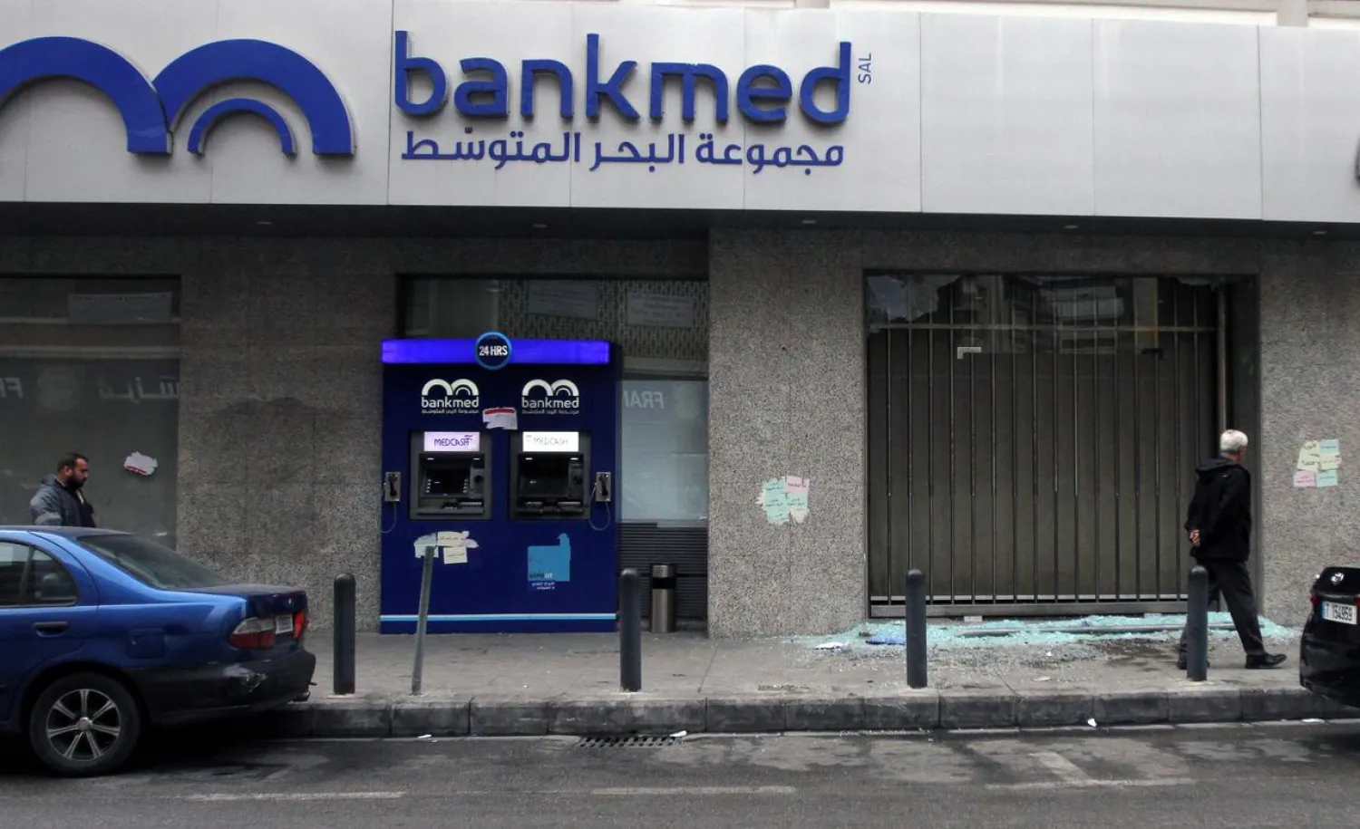 Men walk near broken glass from a damaged Bankmed branch in Tripoli, Lebanon November 27, 2019. REUTERS/Omar Ibrahim