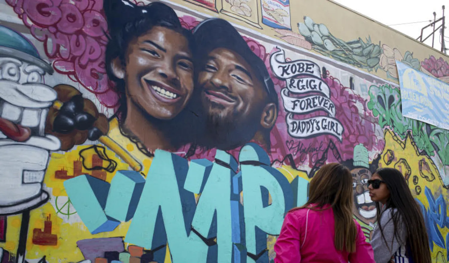 فتاتان تقفان أمام جدارية رُسمت تخليداً للأسطورة كوبي براينت وابنته جيانا في لوس أنجيلس (أ.ب)
