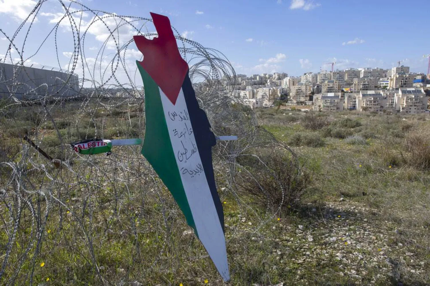 Protesters post a placard with the colors of the Palestinian flags and Arabic that reads "Jerusalem is the eternal capital of Palestine," at a barbed wire surrounding the Israeli separation wall and the Israeli settlement of Mod'in Ilit, background, during a protest against Israel and the United States in the West Bank village of Bil'in, near Ramallah, Friday, Jan. 31, 2020. (AP Photo/Nasser Nasser)