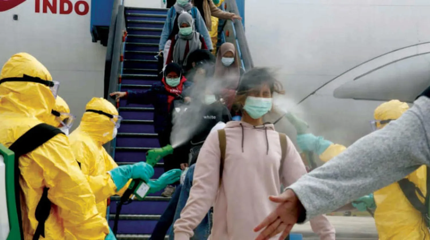 طاقم طبي يعقّم مواطنين إندونيسيين عادوا من ووهان أمس (رويترز)
