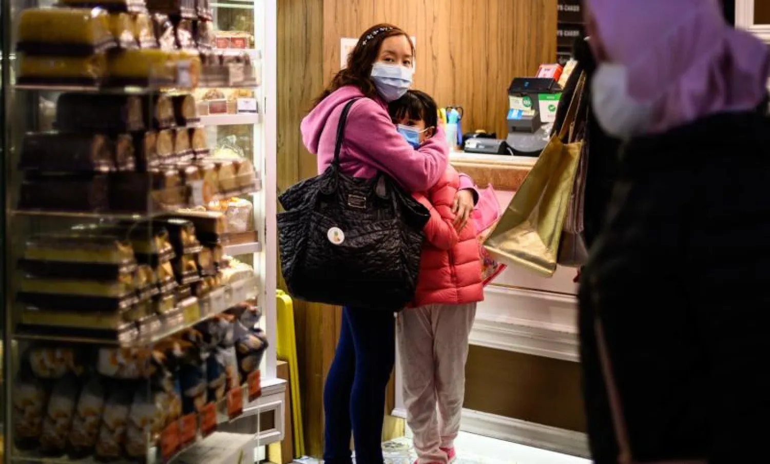 سيدة وطفلتها ترتديان قناعين واقيين بأحد المخابز في هونغ كونغ (أ.ف.ب)