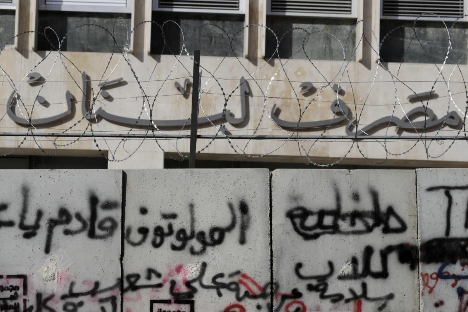 A graffiti that reads in Arabic, "Molotov cocktails are coming," has been painted on a concrete wall installed by authorities to keep anti-government protesters far from the main entrance of the Central Bank, background, during ongoing protests against the Lebanese government, in Beirut, Lebanon, Saturday, Feb. 1, 2020. (AP)