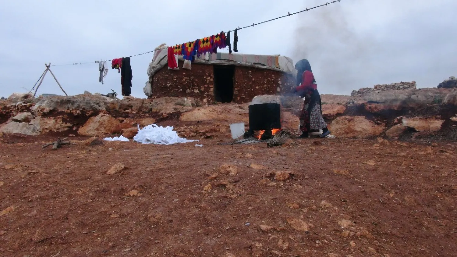 A displaced Syrian builds a fire in a refugee camp. (Asharq Al-Awsat)