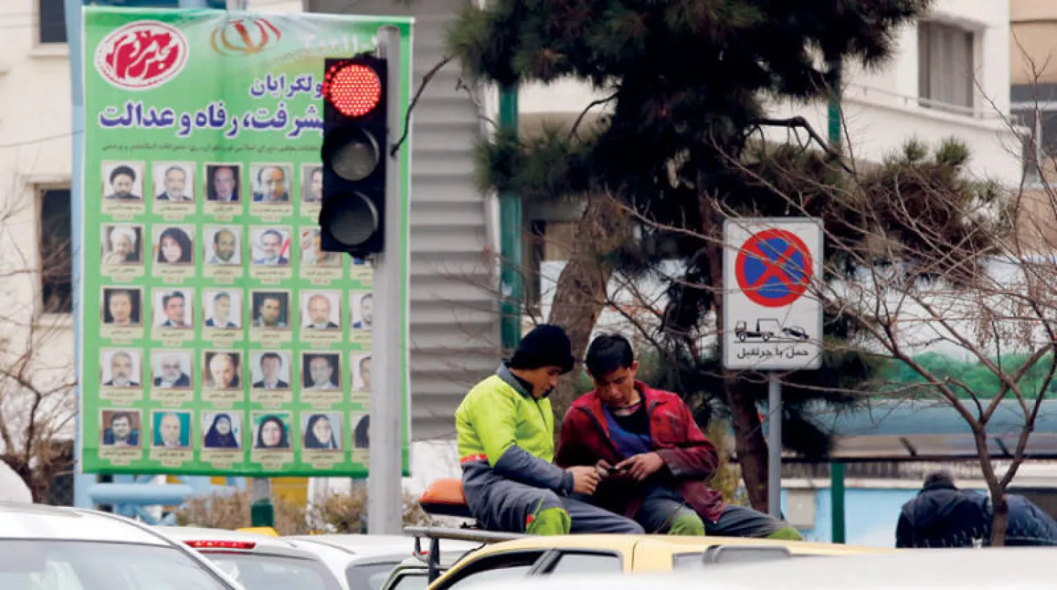 عاملان فوق شاحنة تمر من أمام لافتة دعائية تبرز شعار «التقدم والعدالة والرفاه» فوق قائمة المحافظين في طهران أمس