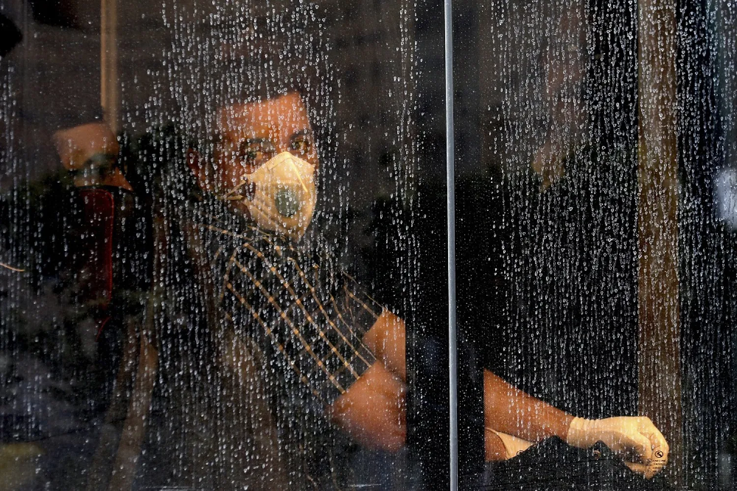 A commuter looks through a water-stained window wearing a mask and gloves to help guard against the coronavirus, on a public bus in downtown Tehran, Iran, Feb. 23, 2020. (AP)