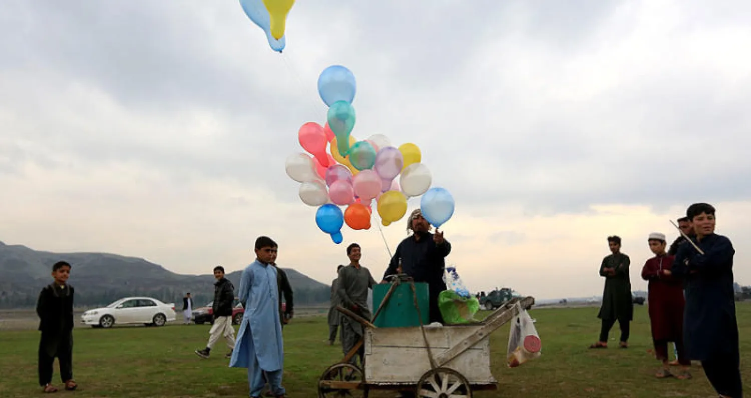 أفغاني يبيع بالونات بينما يحتفل آخرون بخفض التصعيد في جلال آباد أمس (رويترز)