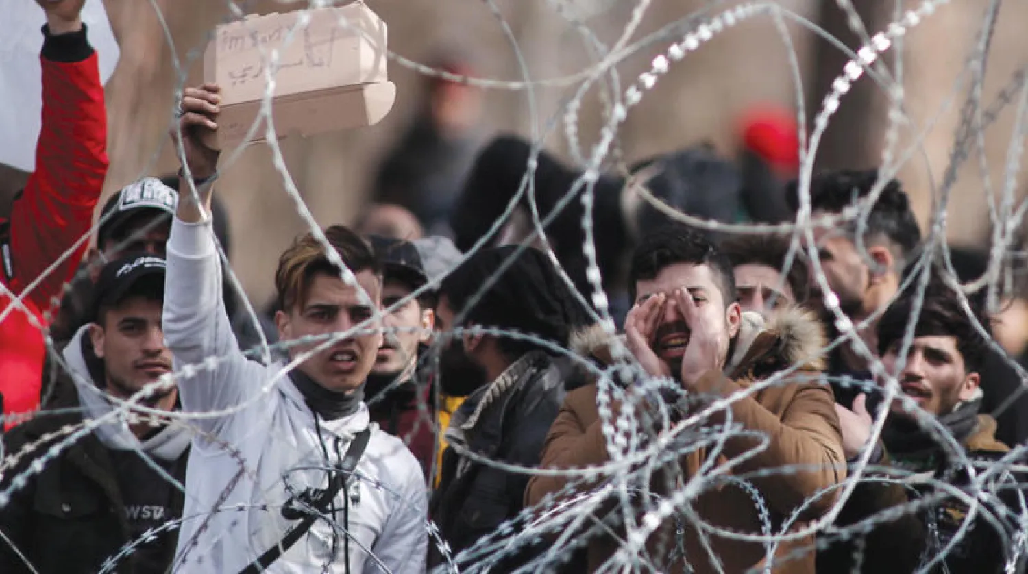 لاجئ ضمن مهاجرين ولاجئين يرفع لافتة على الحدود التركية - اليونانية تقول إنه سوري (إ.ب.أ)