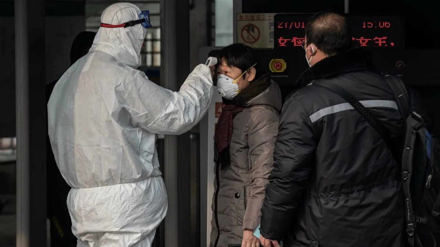 Security personnel wearing protective clothing check the temperature of commuters in Beijing, China, on January 27, 2020. (AFP)