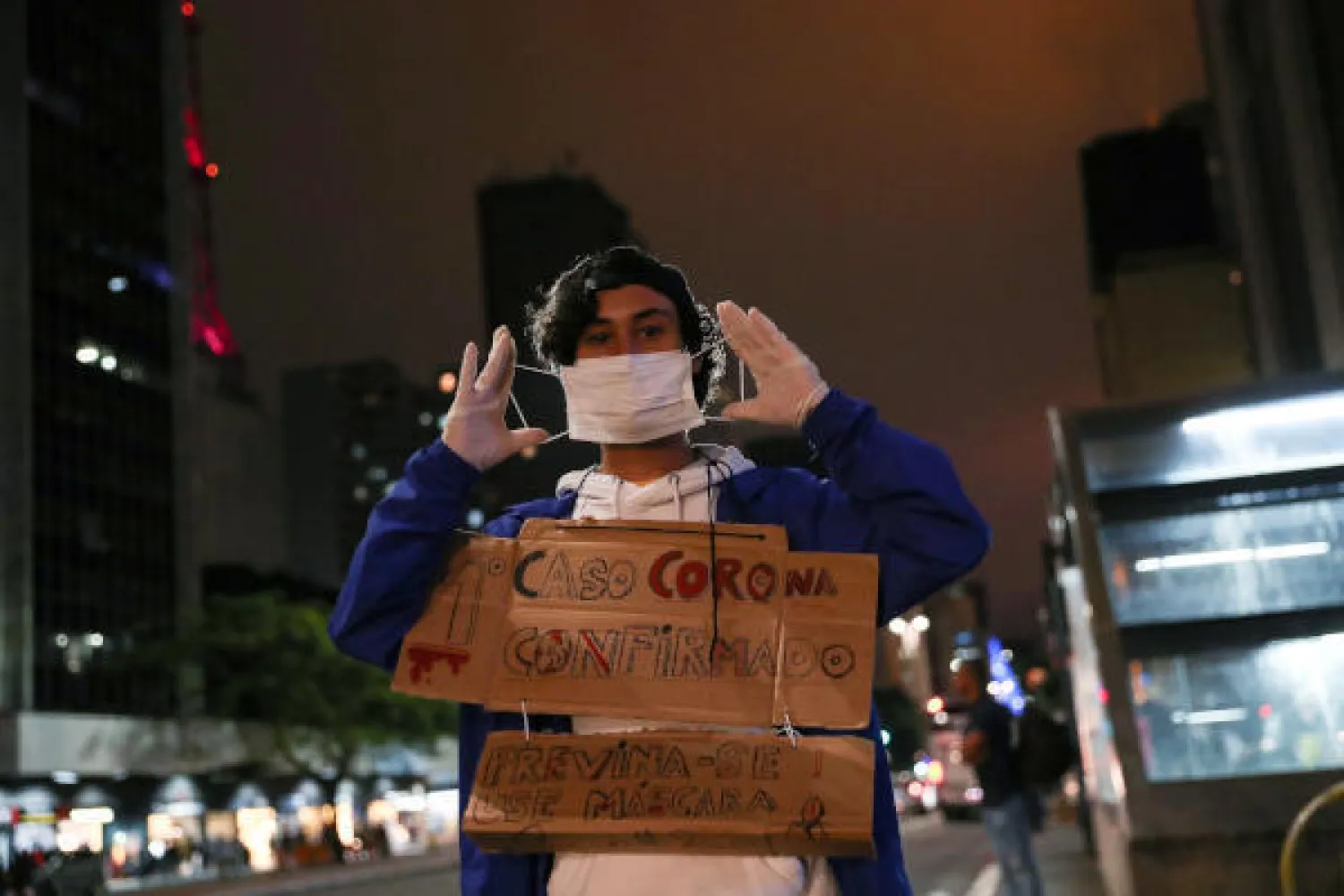 طالب برازيلي يبيع الكمامات بمحطة في ساو باولو ويحمل لافتة تدعو للوقاية من كورونا عبر ارتداء الكمامات (رويترز)