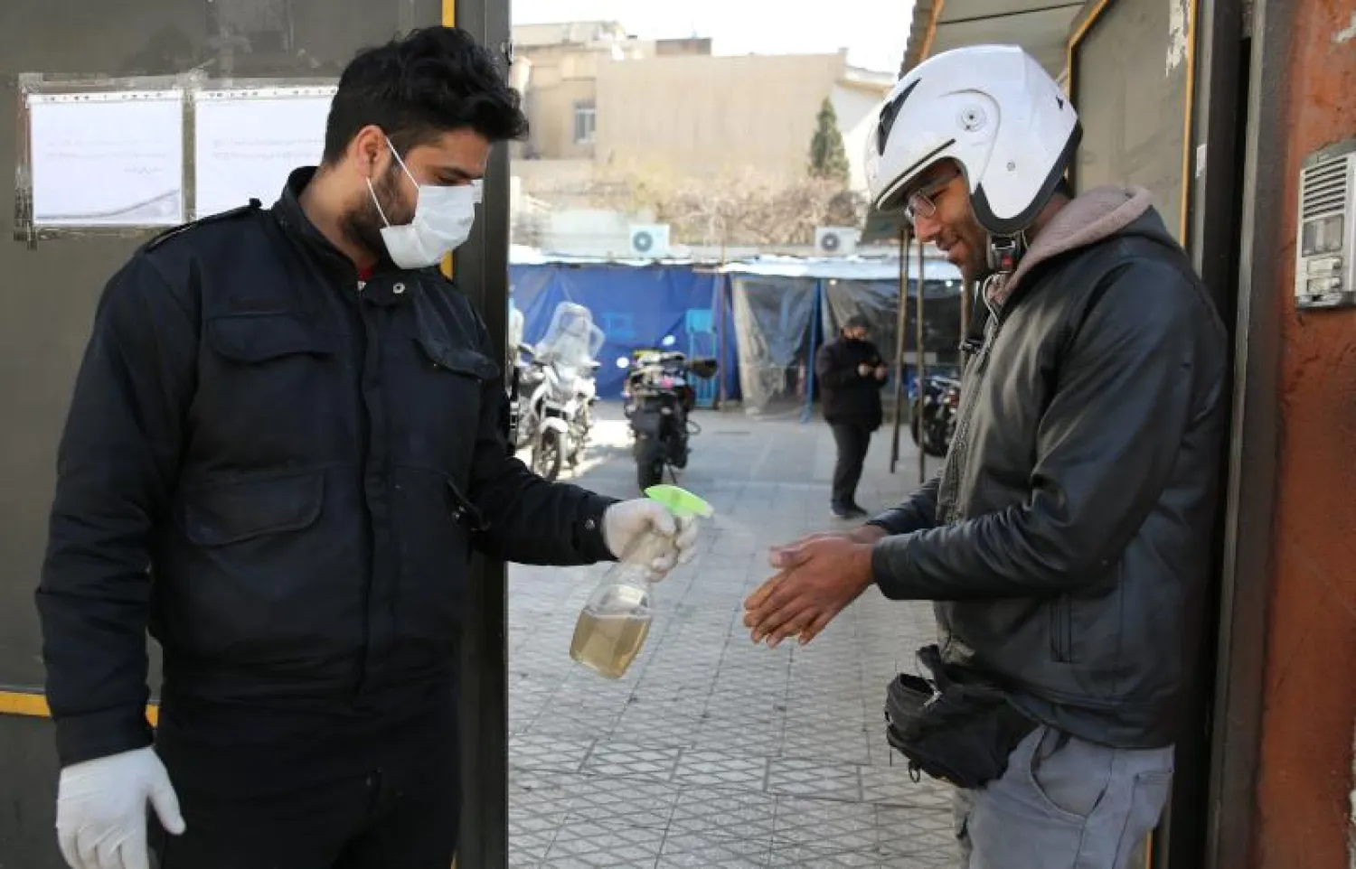 مواطن إيراني يقوم برش مطهر الكحول على يد مواطن آخر في طهران  (أ.ف.ب)