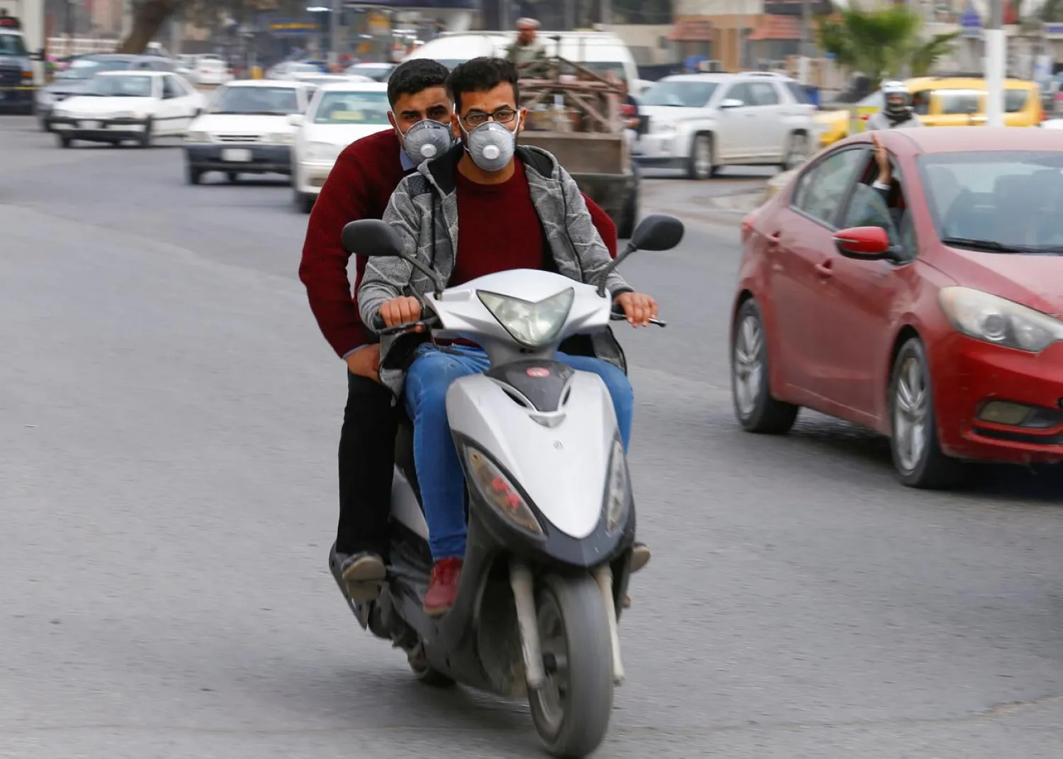 FILE PHOTO: Iraqi men ride a motorbike as they wear protective masks, following the outbreak of the new coronavirus, in Najaf, Iraq February 24, 2020. REUTERS/Alaa al-Marjani