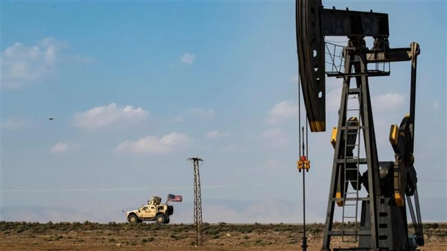 A US military vehicle, part of a convoy arriving from northern Iraq, drives past an oil pump jack in Syria on October 26, 2019. (Photo by AFP)
