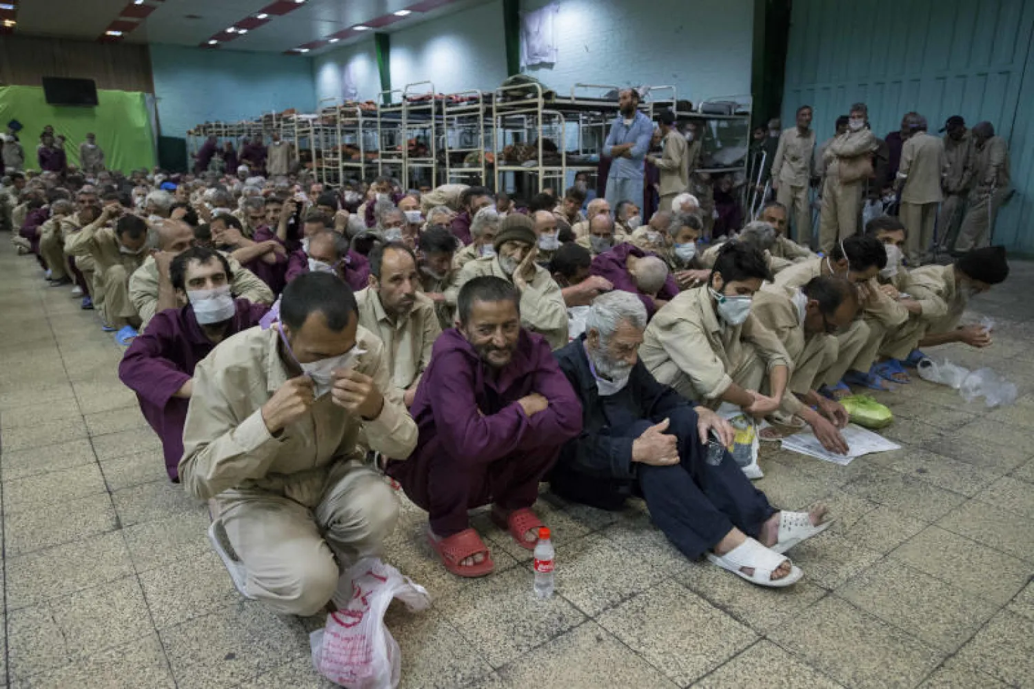 مشردون إيرانيون في مركز إيواء بعد توزيع كمامات عليهم (أ.ب.إ)
