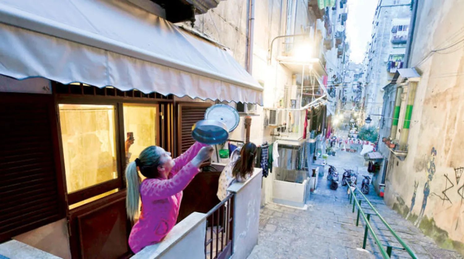 فتاة تشارك جيرانها في الغناء وقرع الآنية في أحد شوارع نابولي (إ.ب.أ)