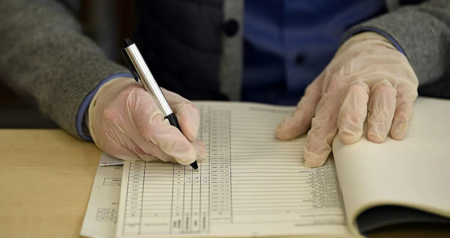 موظف يرتدي قفازات في إجراء احترازي من فيروس «كورونا» لدى تسجيله عمليات الاقتراع بمدينة ميونيخ أمس (رويترز)