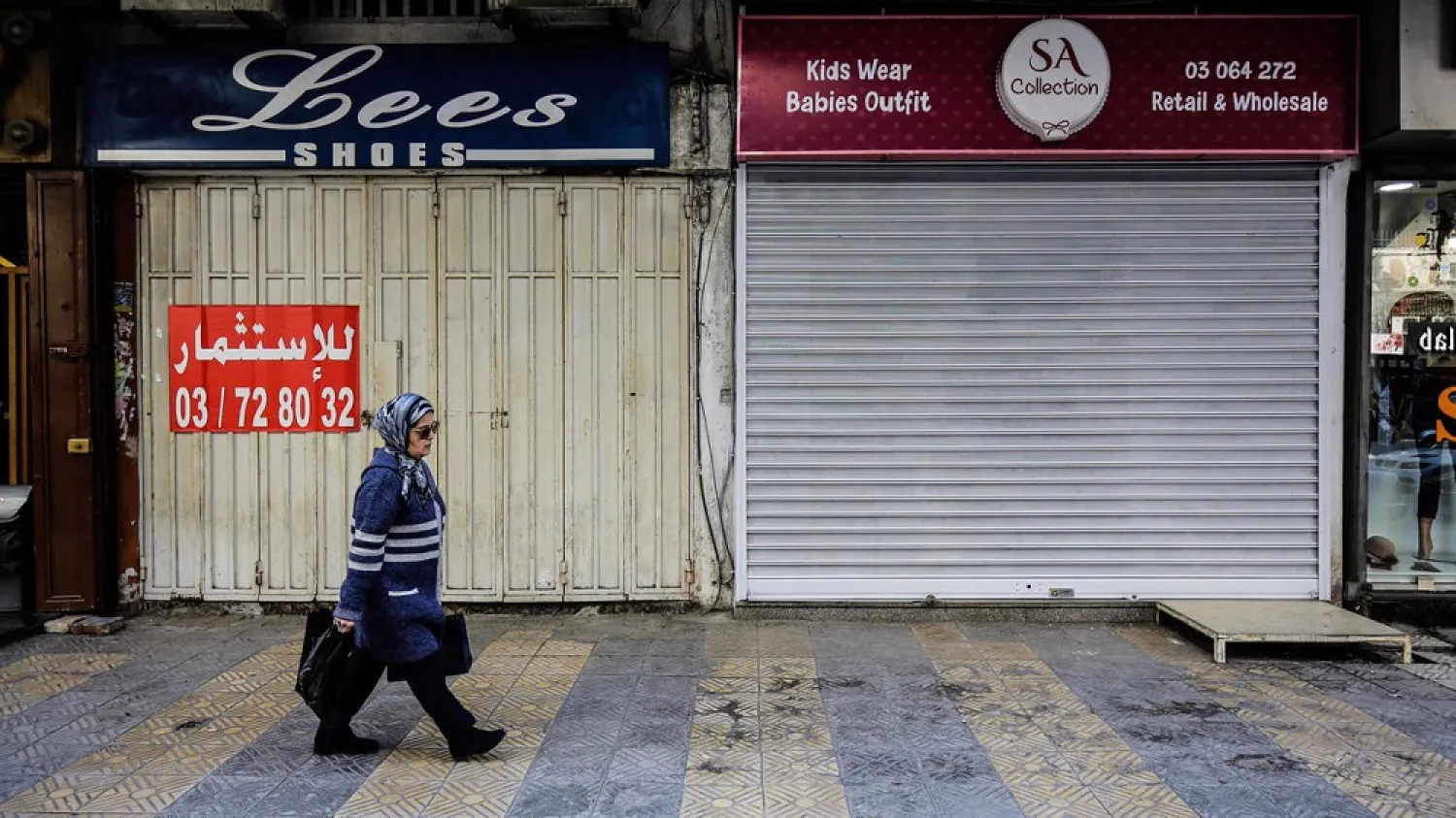A Lebanese woman walks past shuttered stores in the northern city of Tripoli. (AFP)
