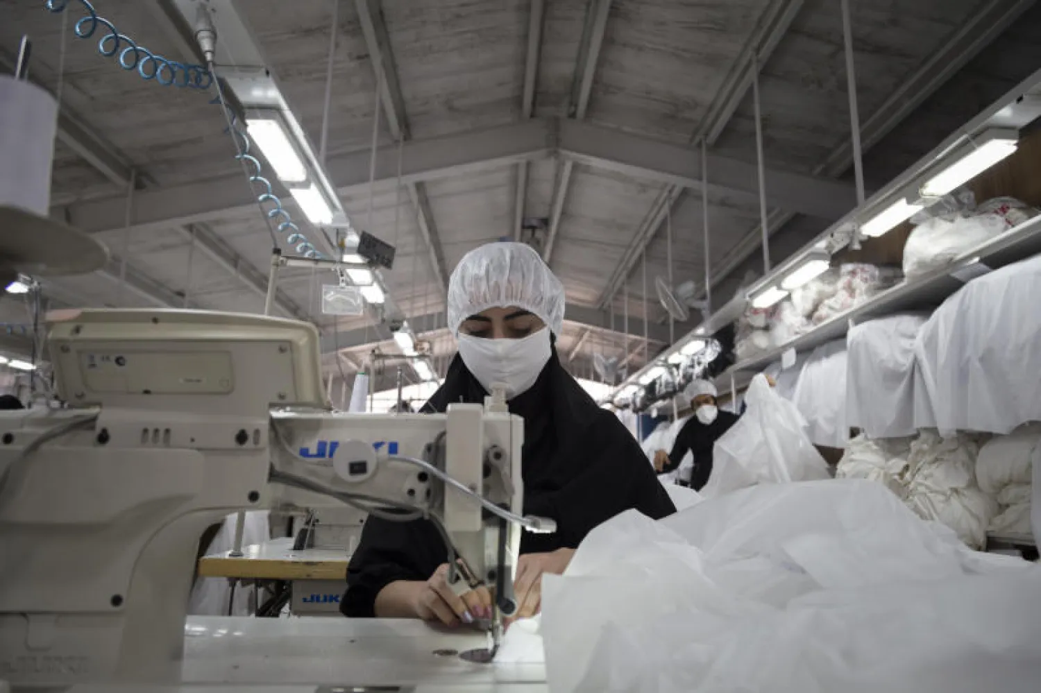 امرأة إيرانية ترتدي قناعاً واقياً تعمل في ورشة خياطة لإنتاج الملابس الواقية الطبية في طهران (د.ب.أ)