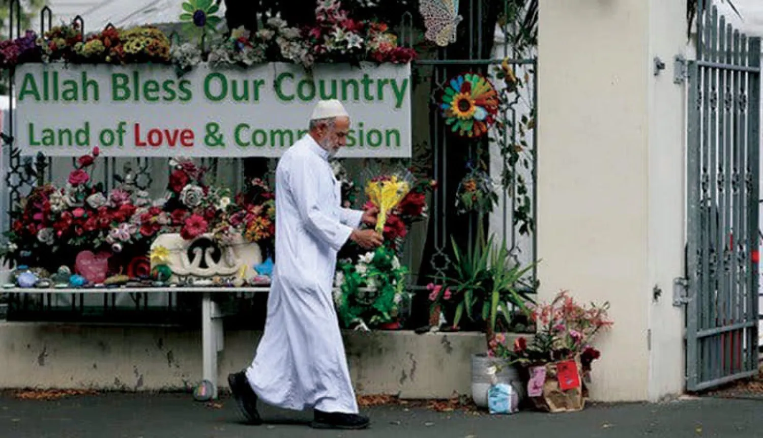 مواطن نيوزيلندي يضع إكليلاً من الورود أمام بوابة مسجد النور الذي تعرض لهجوم إرهابي بكرايست تشيرش في مارس 2019 (غيتي)