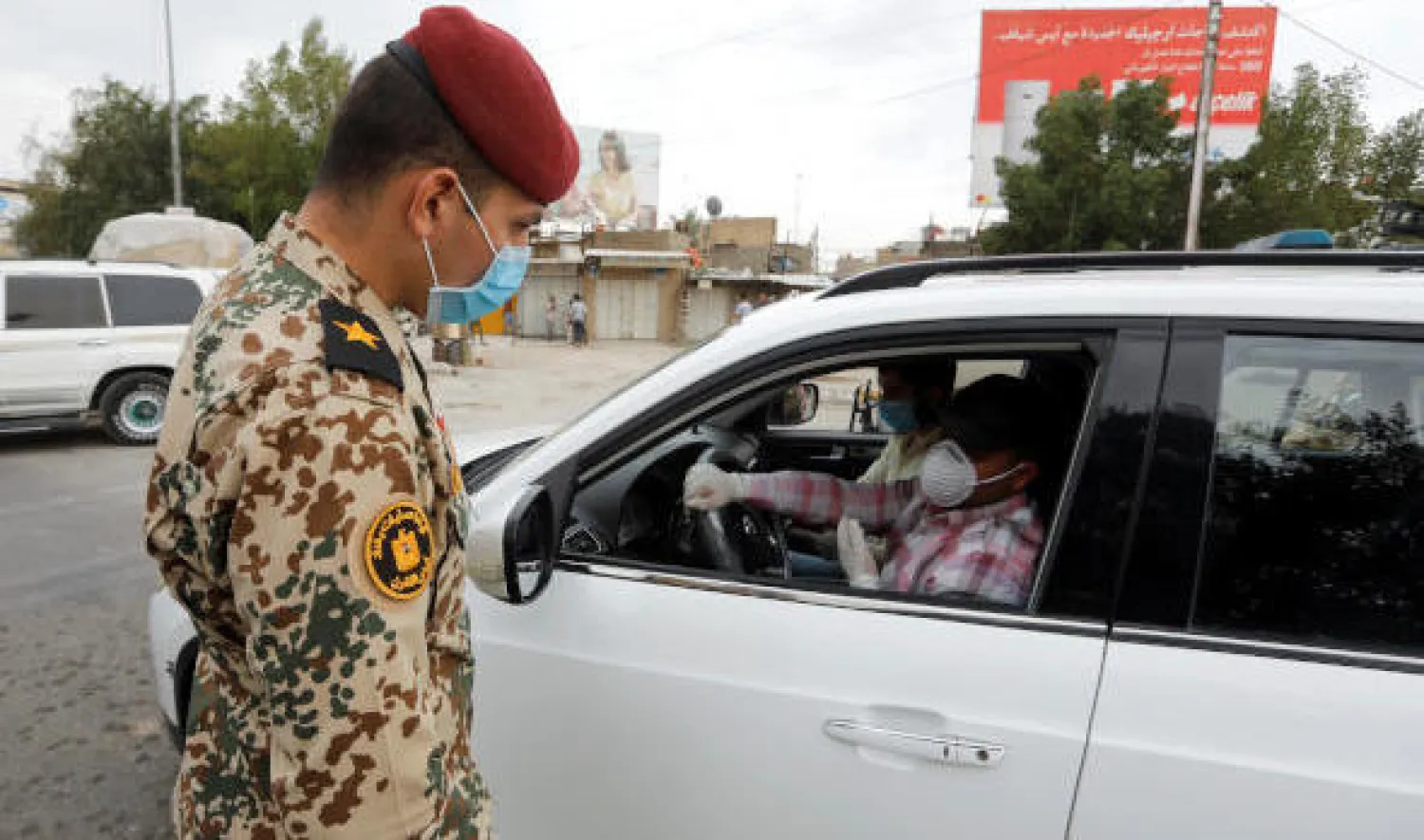 أحد عناصر الجيش العراقي يرتدي كمامة واقية يستوقف سائقاً خلال حظر تجول في بغداد (رويترز)