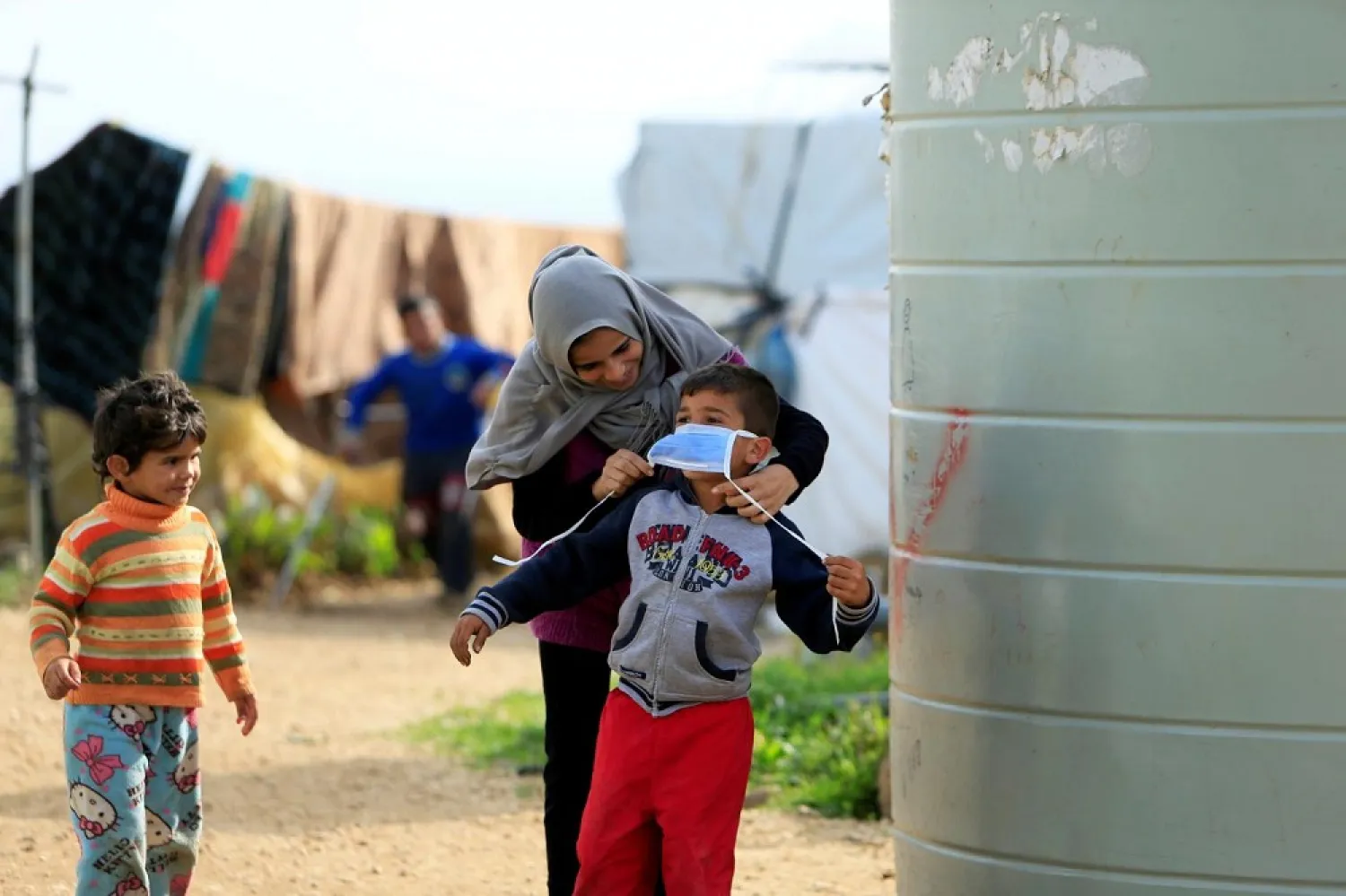 A Syrian refugee helps a child put on a face mask in al-Wazzani, southern Lebanon on March 14, 2020. (Reuters)