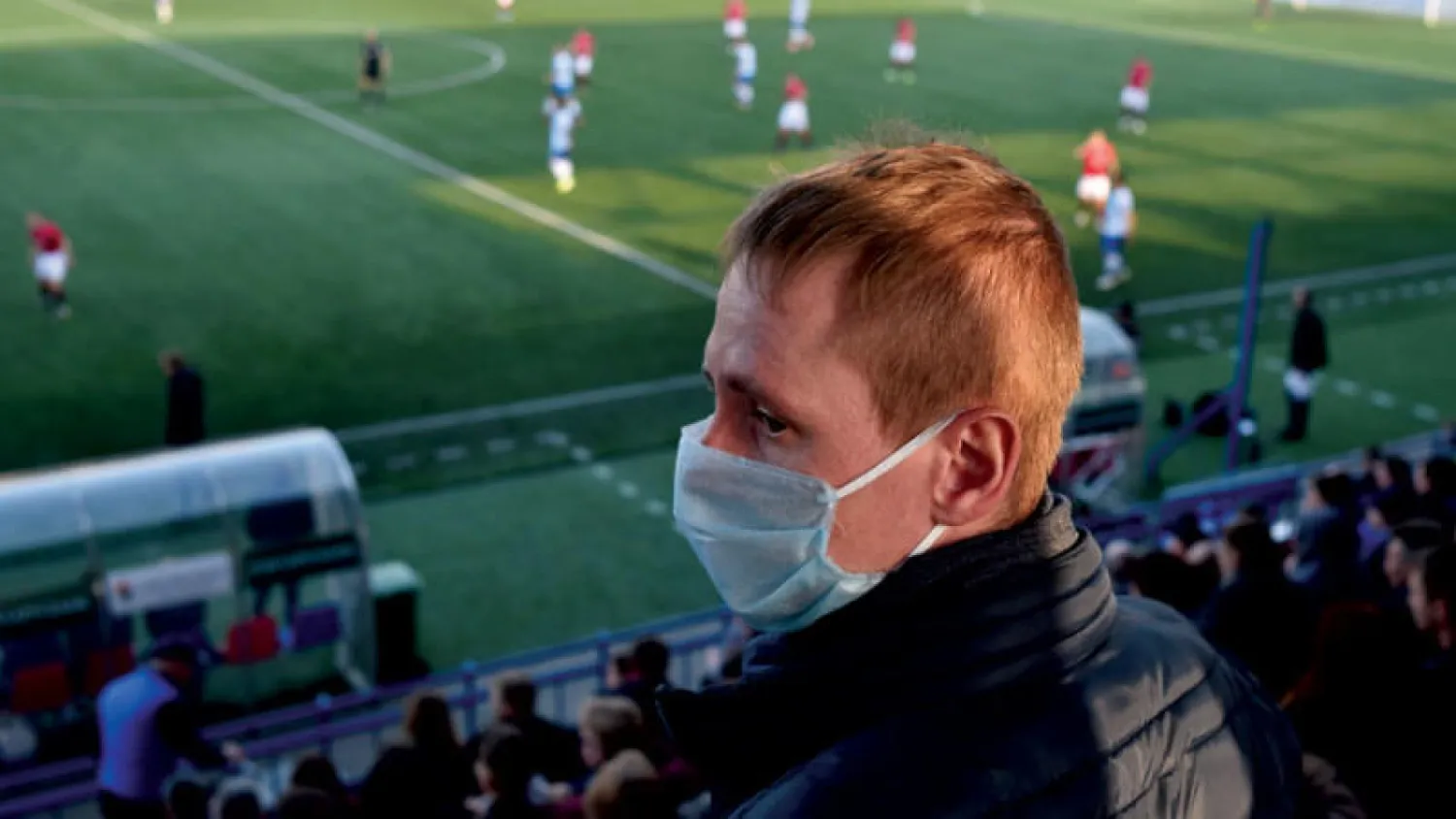 مشجع يرتدي الكمامة لمتابعة مباراة بين فريقي مينسك ودينامو مينسك بدوري روسيا البيضاء (أ.ف.ب)