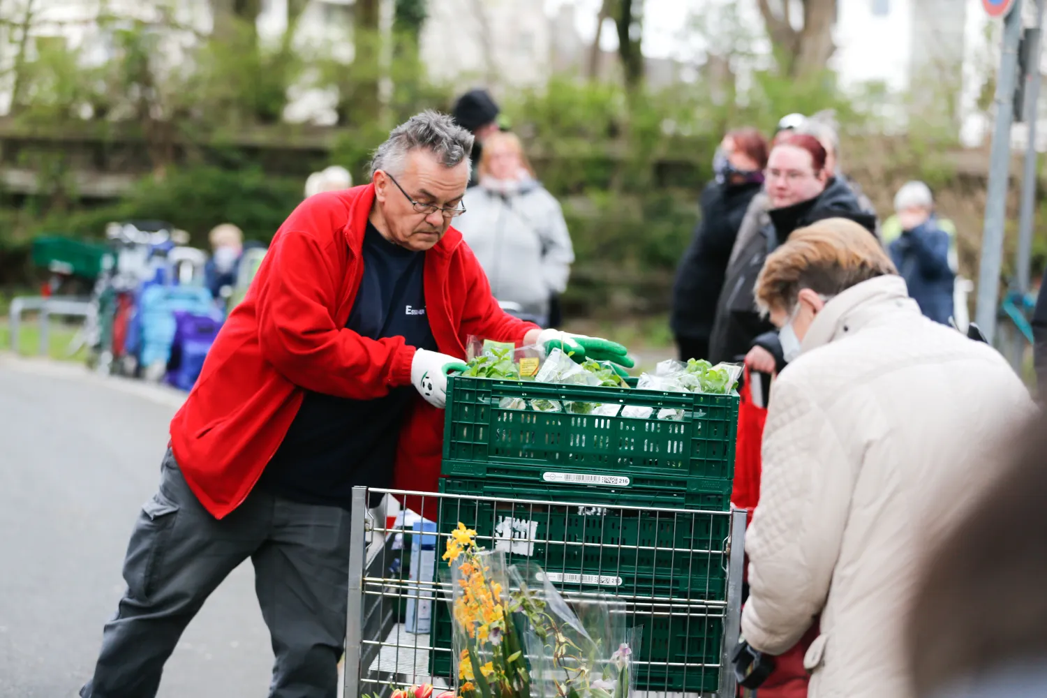 رجل يقوم بتحميل مواد غذائية فيما يصطف آخرون بعربات التسوق عند نقطة توزيع لبنك طعام في مدينة إيسن الألمانية (رويترز)