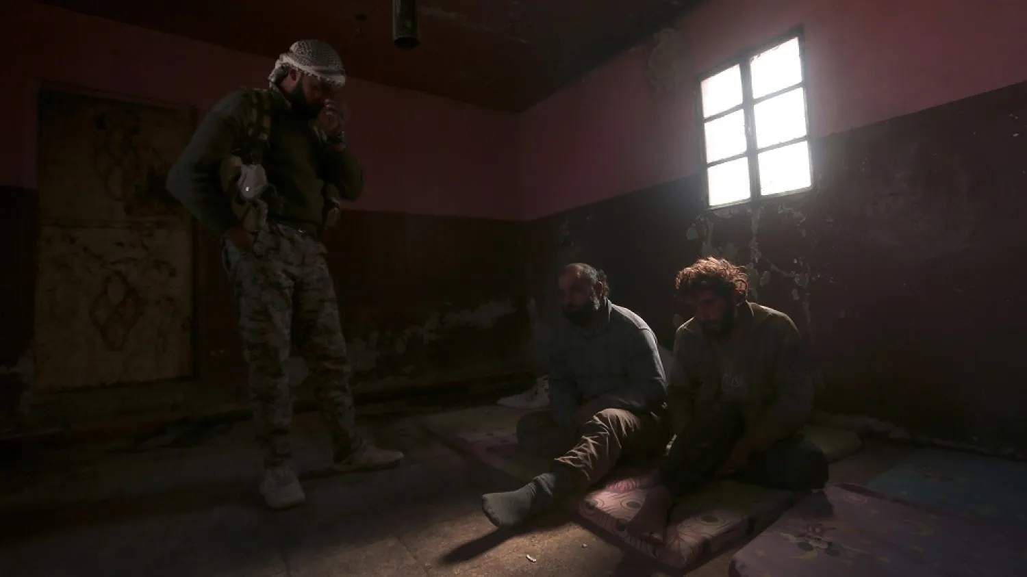 An SDF fighter stands near men he said were ISIS fighters held as prisoners, north of Raqqa, Syria, March 8, 2017. (Reuters)