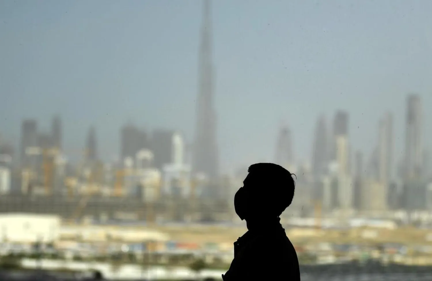 A man wearing a protective mask stands at a racetrack overlooking Dubai. (AFP)