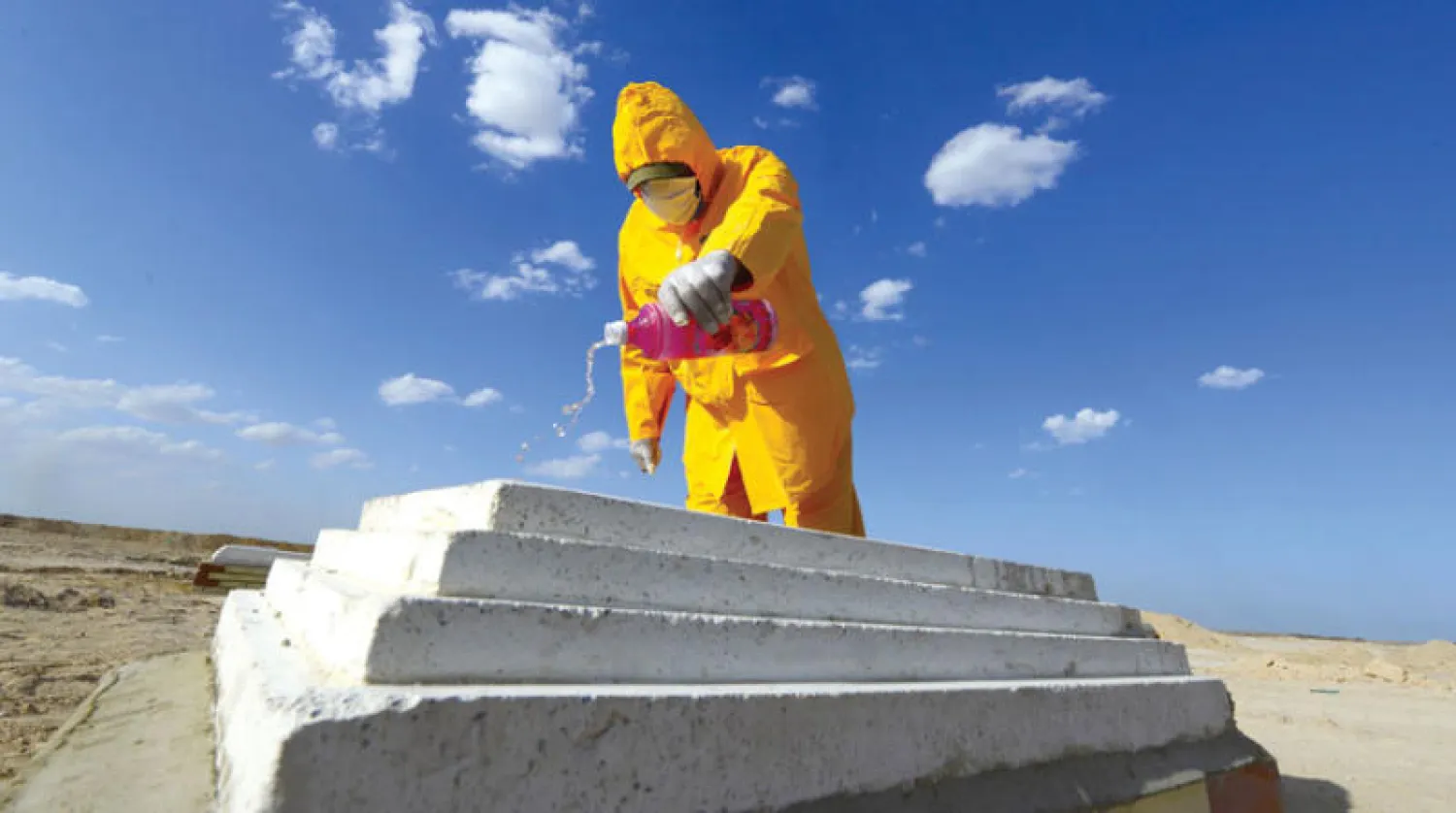 عراقي يصب مطهراً أمس على قبر ضحية لفيروس {كورونا} في مقبرة تبعد 20 كيلومتراً عن النجف (أ.ف.ب)