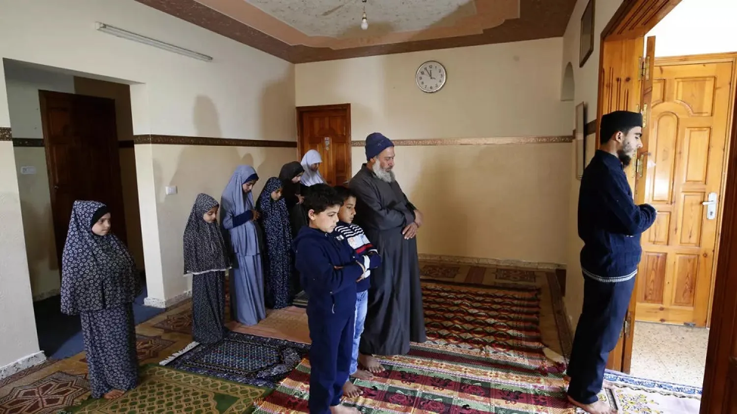 Saleh Shtaiwi (R), a Palestinian weekly prayers leader in a mosque, leads Friday prayers for his family at home in Gaza City. (AFP)