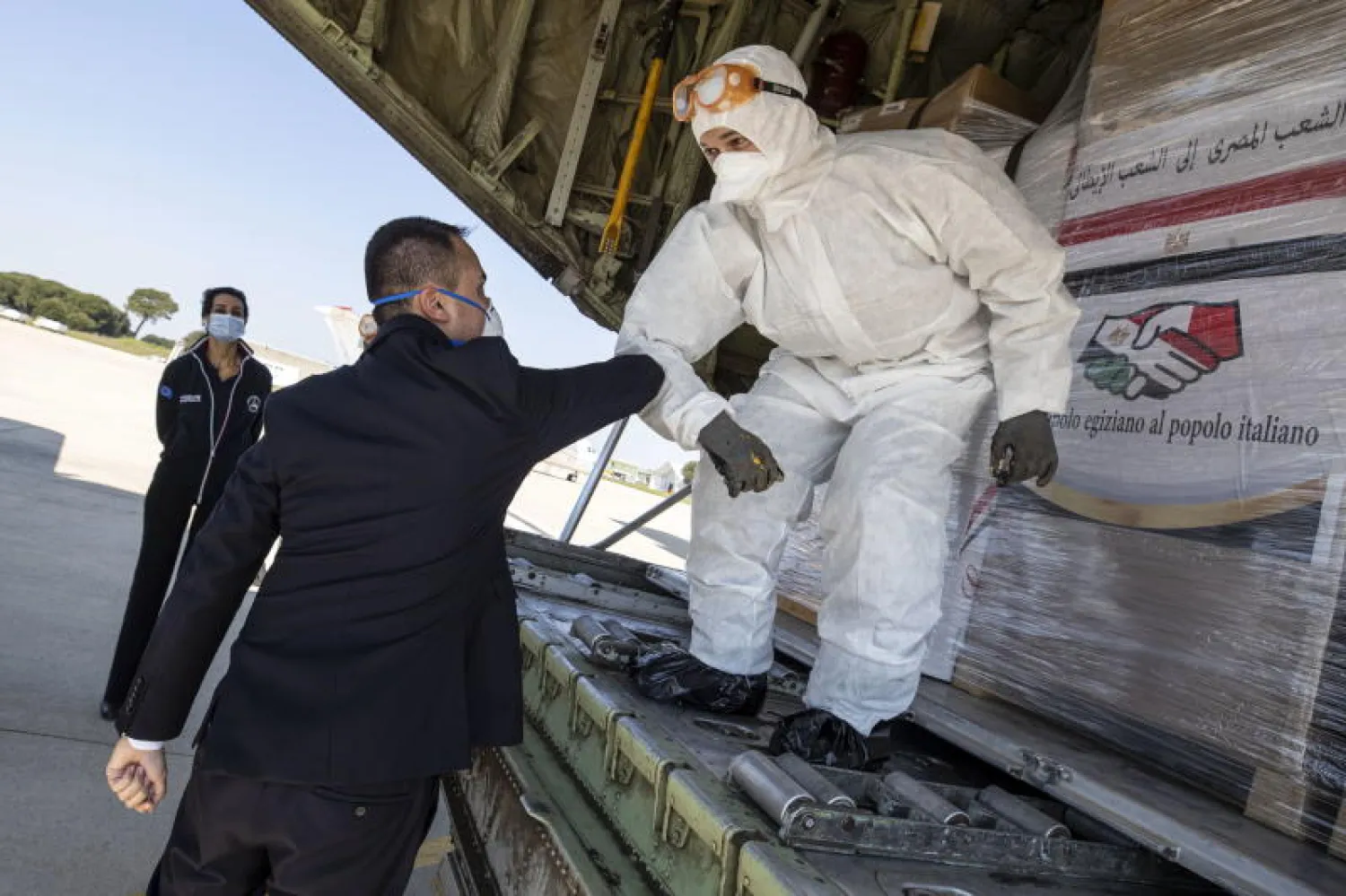 وزير الخارجية الإيطالي يسلم على أحد أفراد طاقمي طائرتين عسكريتين مصريتين تحملان مساعدات طبية (إ.ب.أ)
