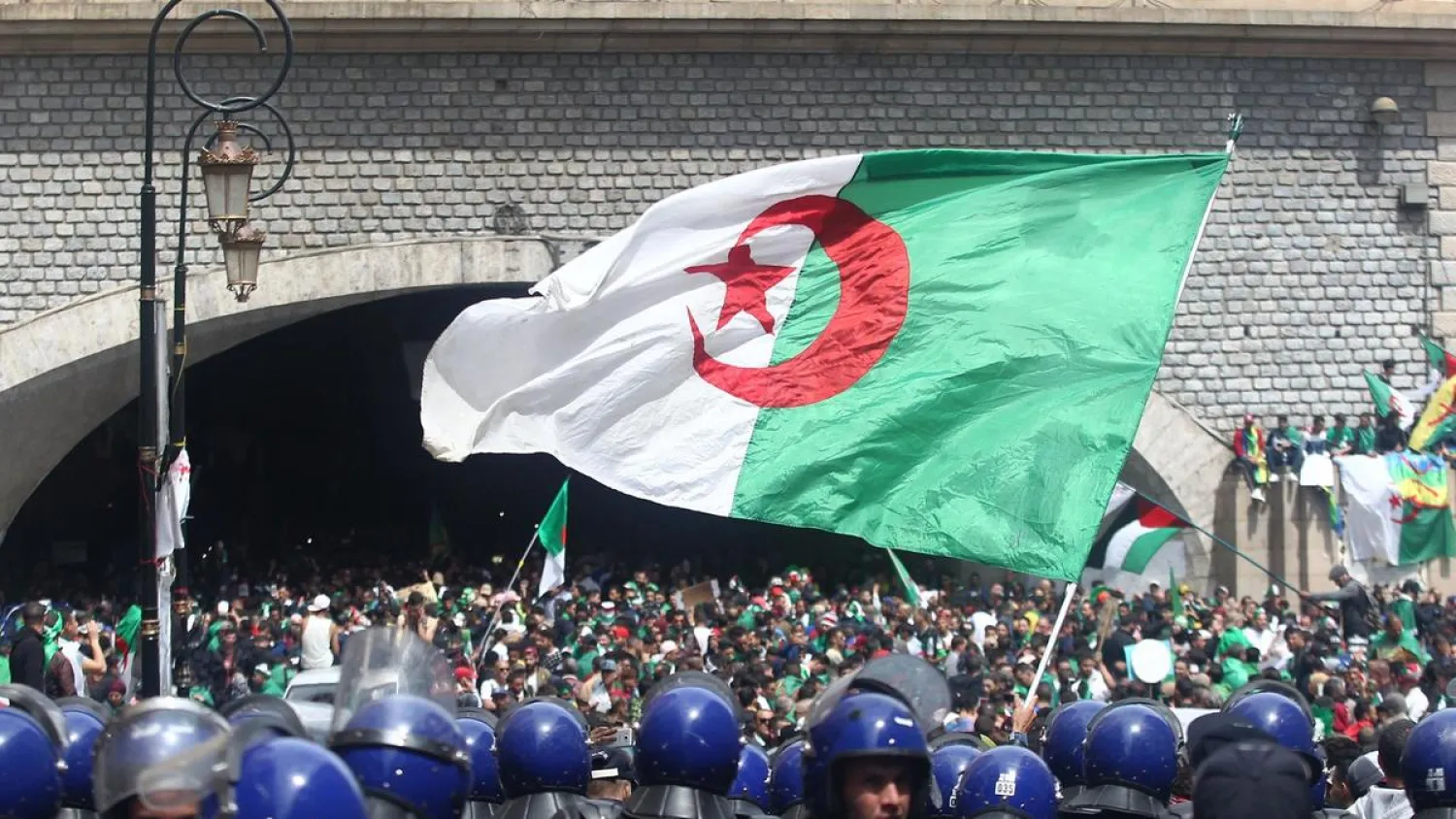Algerian protesters wave a national flag as security forces stand guard during an an anti-government demonstration in Algiers on April 12, 2019. (AFP)