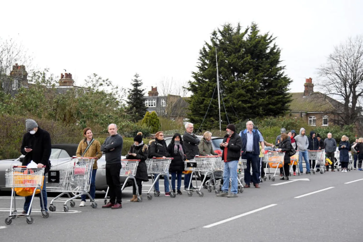متسوقون يحافظون على المسافة الامنة في صف انتظارهم خارج محلات البقالة (رويترز)