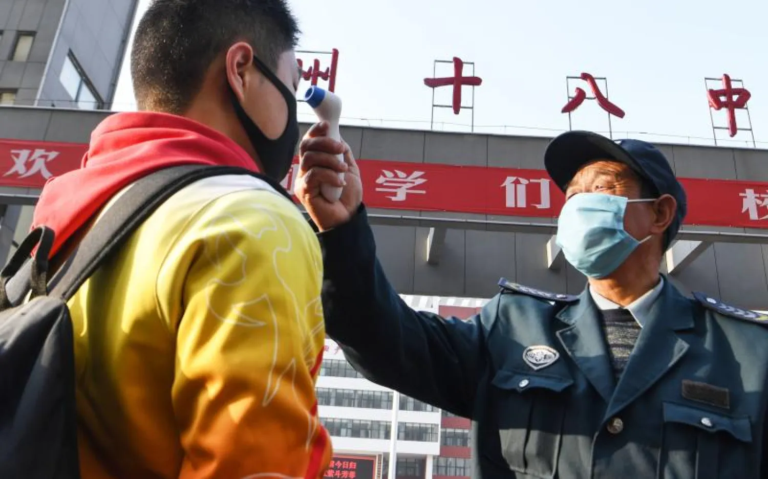 موظف يفحص تلميذ مدرسة خوفاً من فيروس كورونا في الصين (أ.ف.ب)