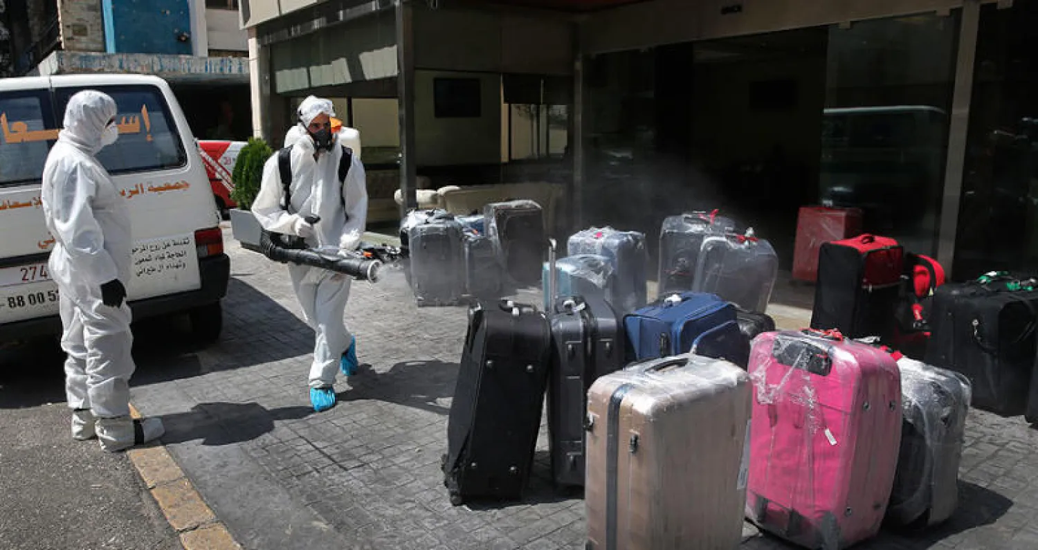 عامل يعقّم أمتعة لبنانيين عائدين من الخارج في بيروت أمس (أ.ب)