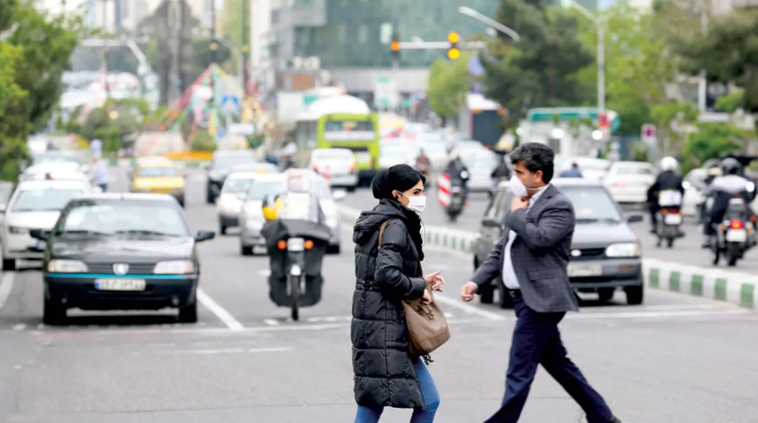 إيرانيان يرتديان الكمامة يعبران طريقاً رئيسية في طهران أمس (أ.ف.ب)