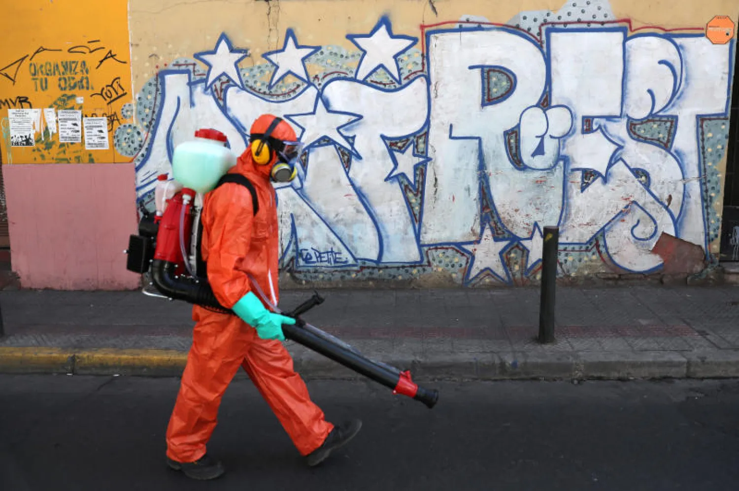 عامل يرتدي بدلة واقية خلال تطهير شارع بحي سكني في سانتياغو عاصمة تشيلي (رويترز)