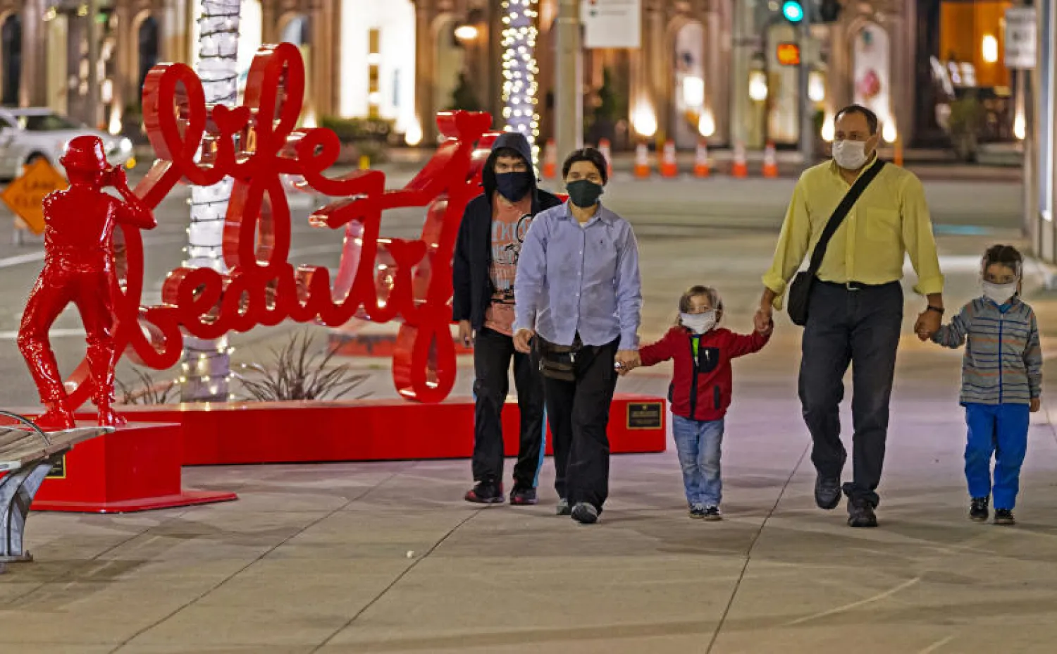 عائلة ترتدي أقنعة وجه واقية بينما تتجول في أحد شوارع بيفيرلي هيلز بكاليفورنيا (أ.ب)