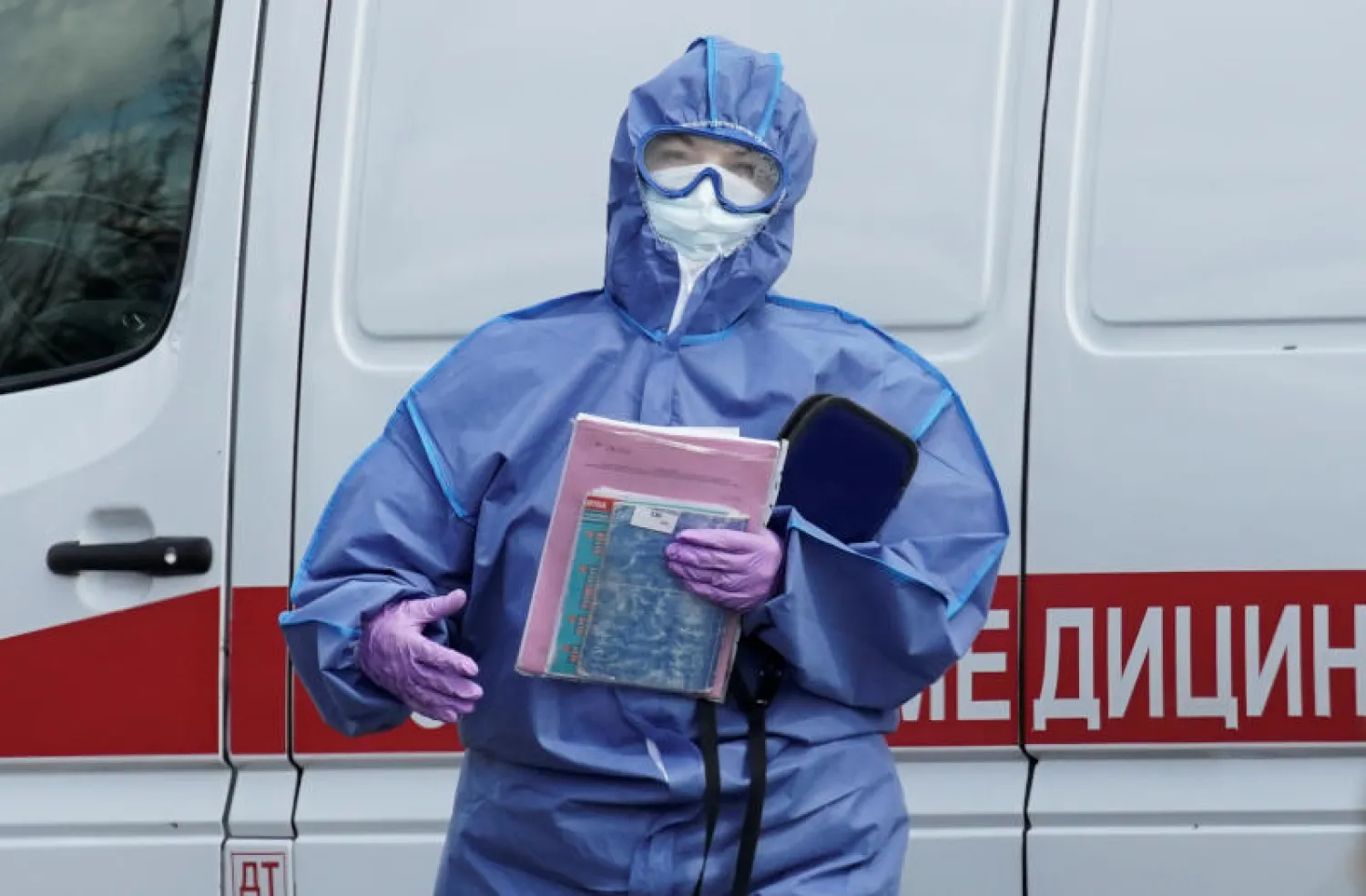 اختصاصي طبي يرتدي ملابس واقية بجوار سيارة إسعاف خارج مستشفى لعلاج مرضى كورونا في موسكو (رويترز)