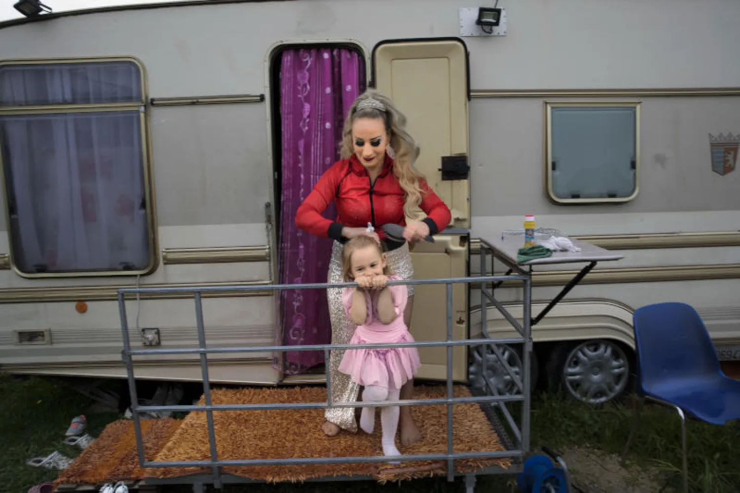 امرأة تسرّح شعر ابنتها خارج العربة التي تقيم فيها العائلة قرب نابولي في جنوب إيطاليا (أ.ب)