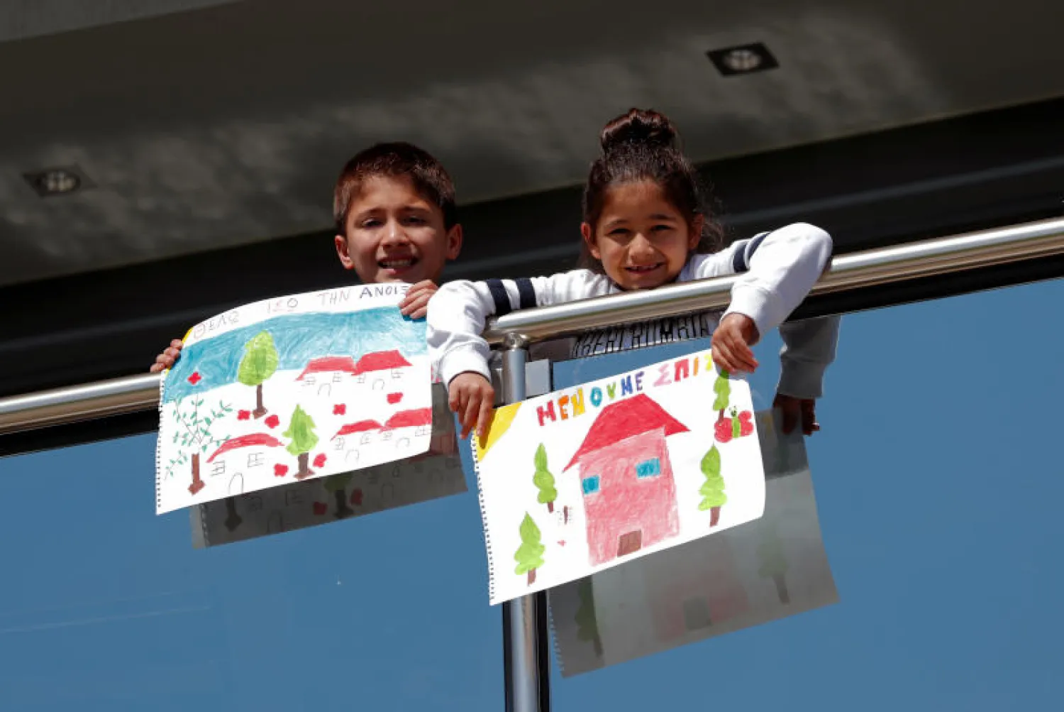 طفلان يونانيان يحملان ما رسماه خلال العزل المنزلي في سالونيكا (رويترز)