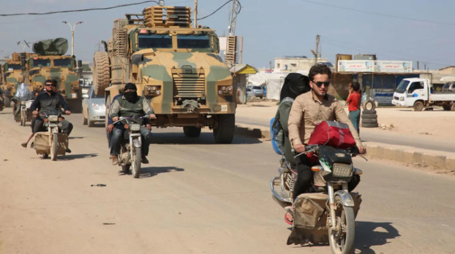 سوريون على دراجات قرب دورية عسكرية تركية في ريف إدلب (أ.ف.ب)