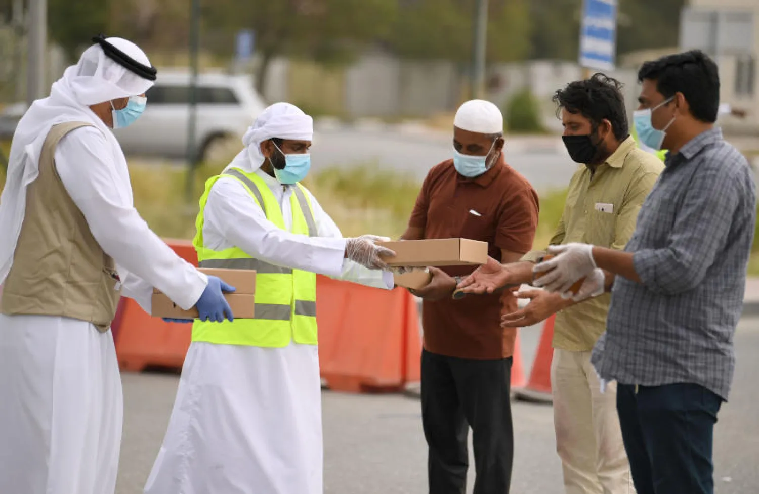 متطوعون يرتدون كمامات يوزعون وجبات إفطار مجانية على عمال أجانب في الإمارات (أ.ف.ب)
