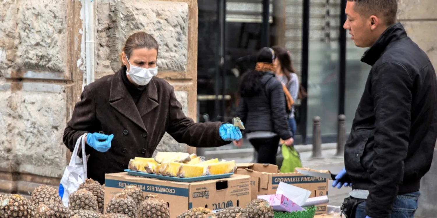 A woman wearing a mask buys pineapple from a fruit vendor in Tunis on March 17, 2020. (AP)
