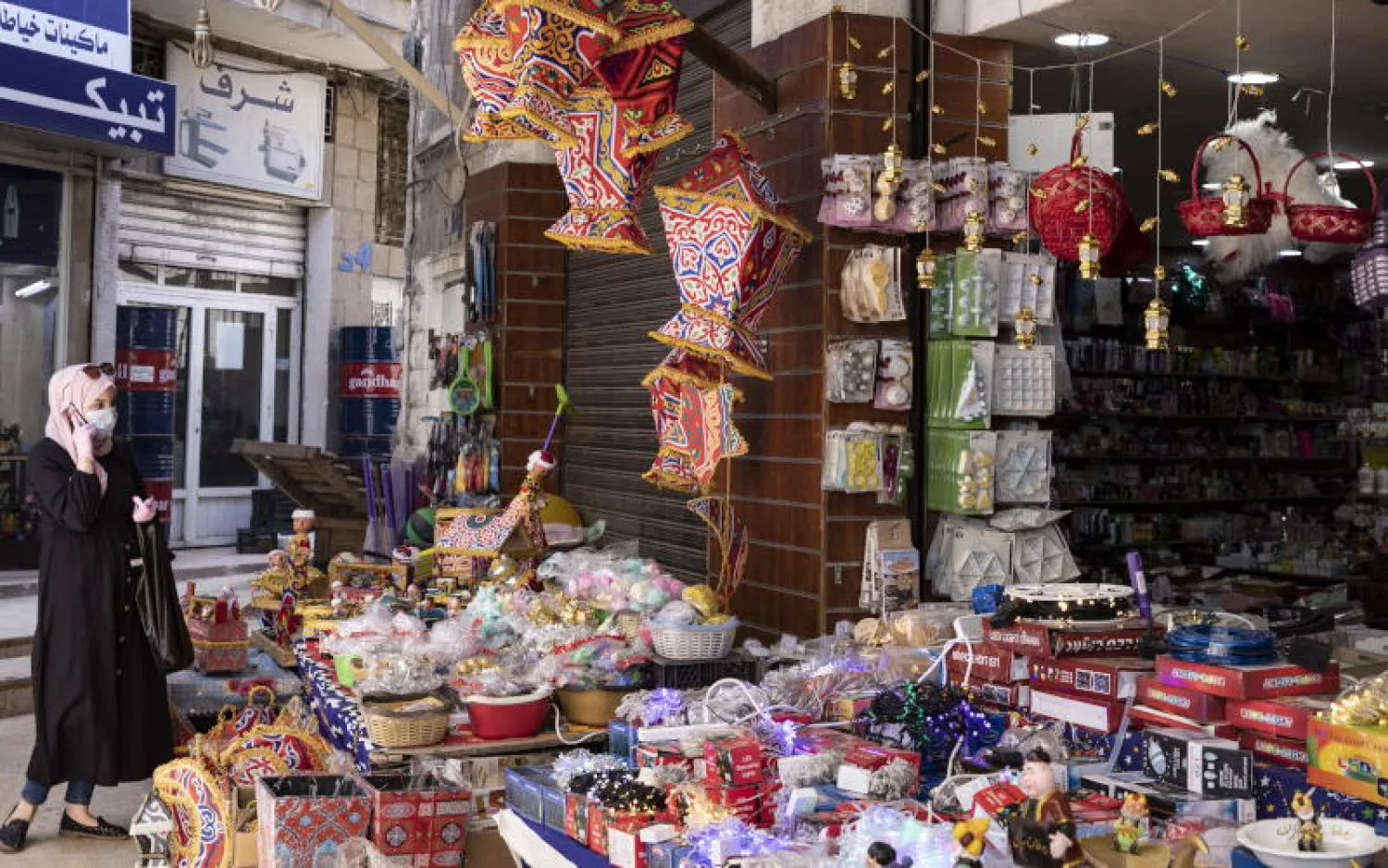 سيدة أردنية ترتدي كمامة أمام متجر أدوات منزلية وزينة رمضان في عمان (إ.ب.أ)